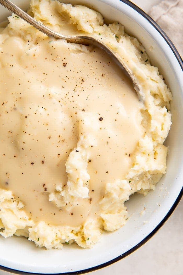 Overhead shot of chicken gravy over mashed potatoes in a white bowl with a spoon