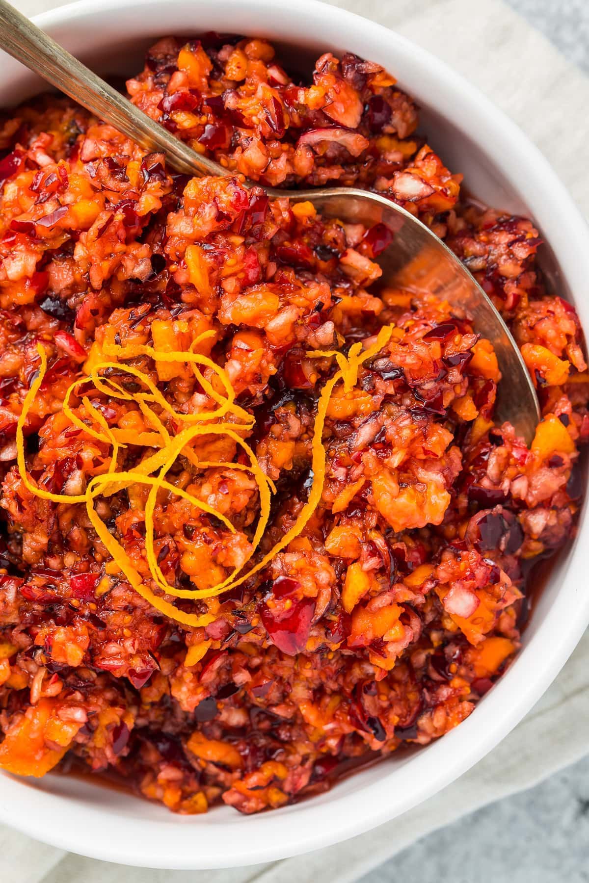 Cranberry orange relish in a white bowl with a silver spoon on a white napkin.