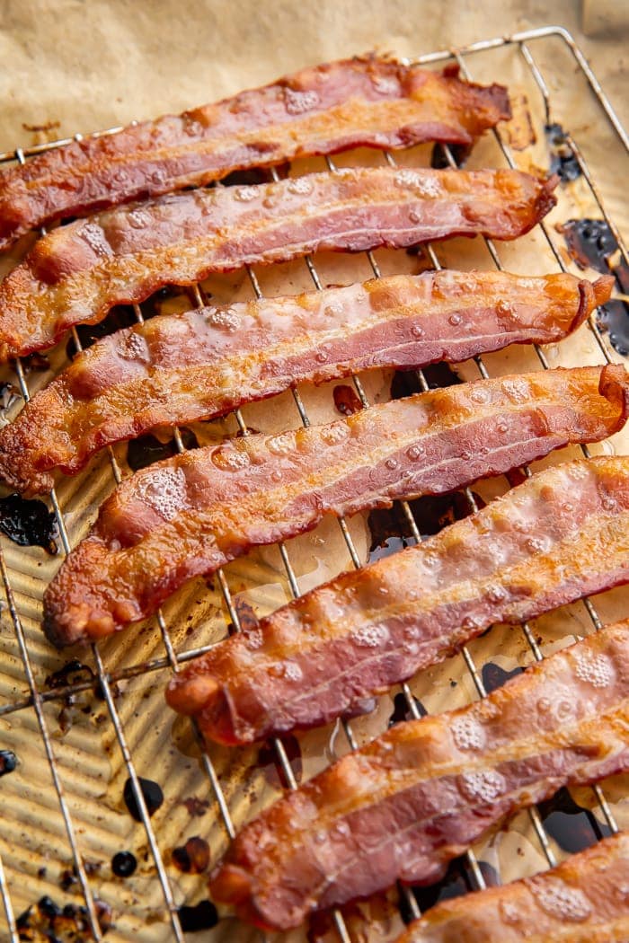 Crispy oven-cooked bacon on a silver cooling rack lined with parchment paper