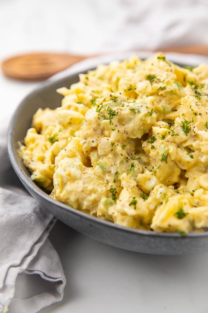 Dark serving bowl with yellow potato salad and green garnish