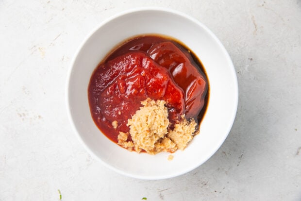 Ketchup, horseradish, and other ingredients for shrimp cocktail sauce in a white bowl on a marble countertop