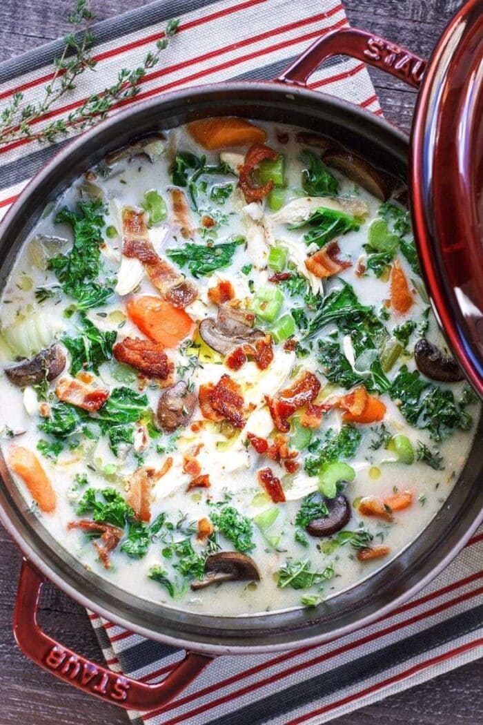 A large red pot of soup with chicken, kale, bacon, and veggies