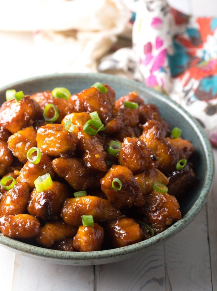 A blue ceramic bowl with glazed Whole30 Firecracker Chicken on a white table 