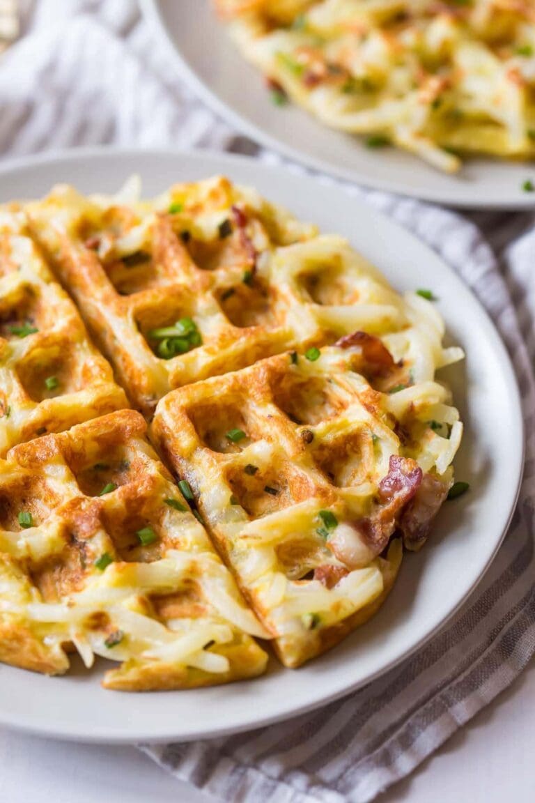 View of hashbrown bacon and egg waffles on white plate.