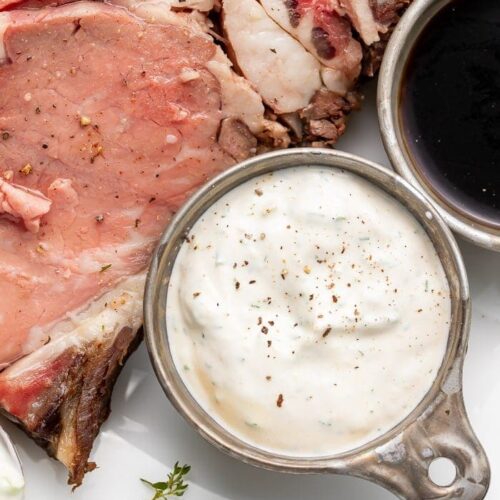 A side of horseradish sauce next to prime rib on a white plate