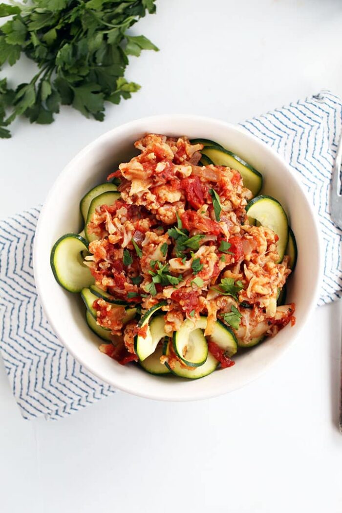 A white bowl of vegetarian slow cooker crockpot cauliflower bolognese on top of zucchini noodles