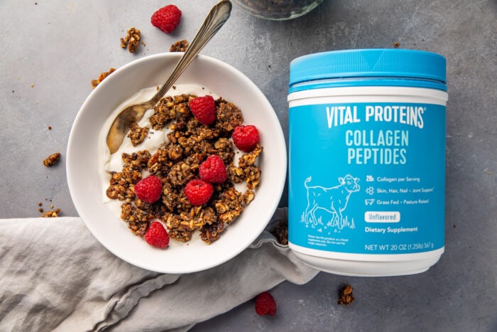 Vital proteins collagen peptides container next to a bowl of yogurt topped with granola and raspberries