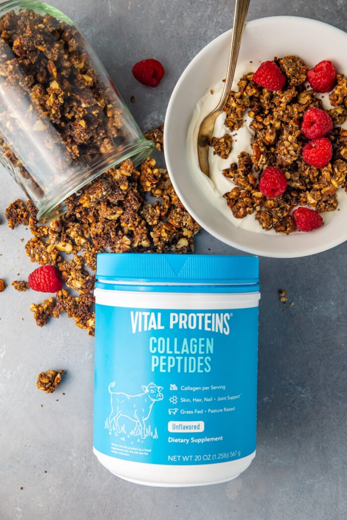 Vital Proteins collagen peptides container next to a glass jar of spilled granola and a bowl of keto granola on top of yogurt with raspberries