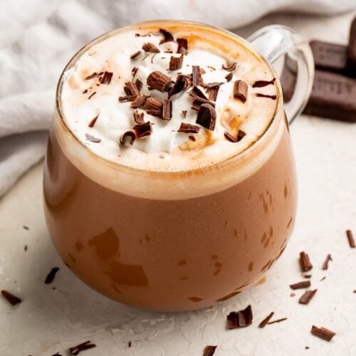 Zoomed out photo of keto hot chocolate with whipped topping and chocolate shavings in a glass mug