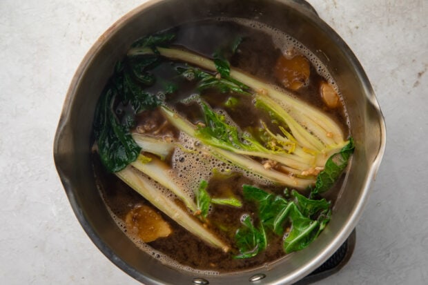 Ramen broth and bok choy in a silver pot