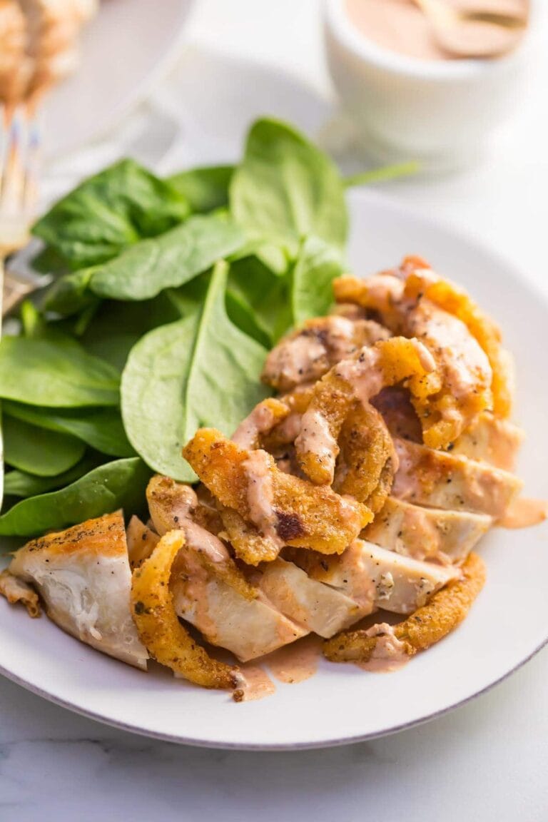 Top view of onion blossom chicken on white plate with spinach leaves.