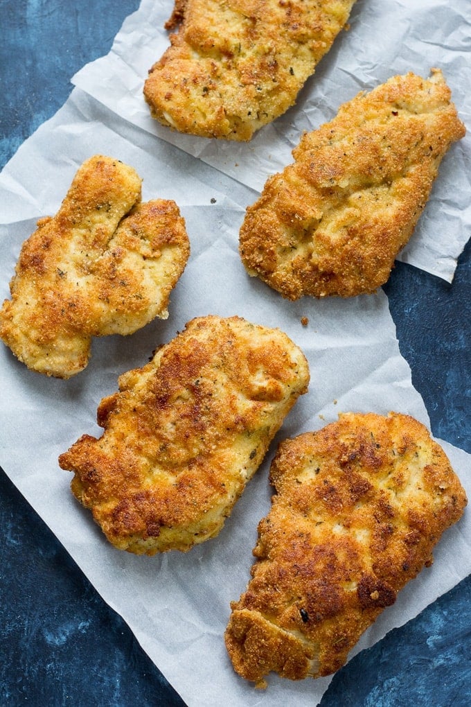 5 breaded chicken cutlets on parchment paper on a blue countertop