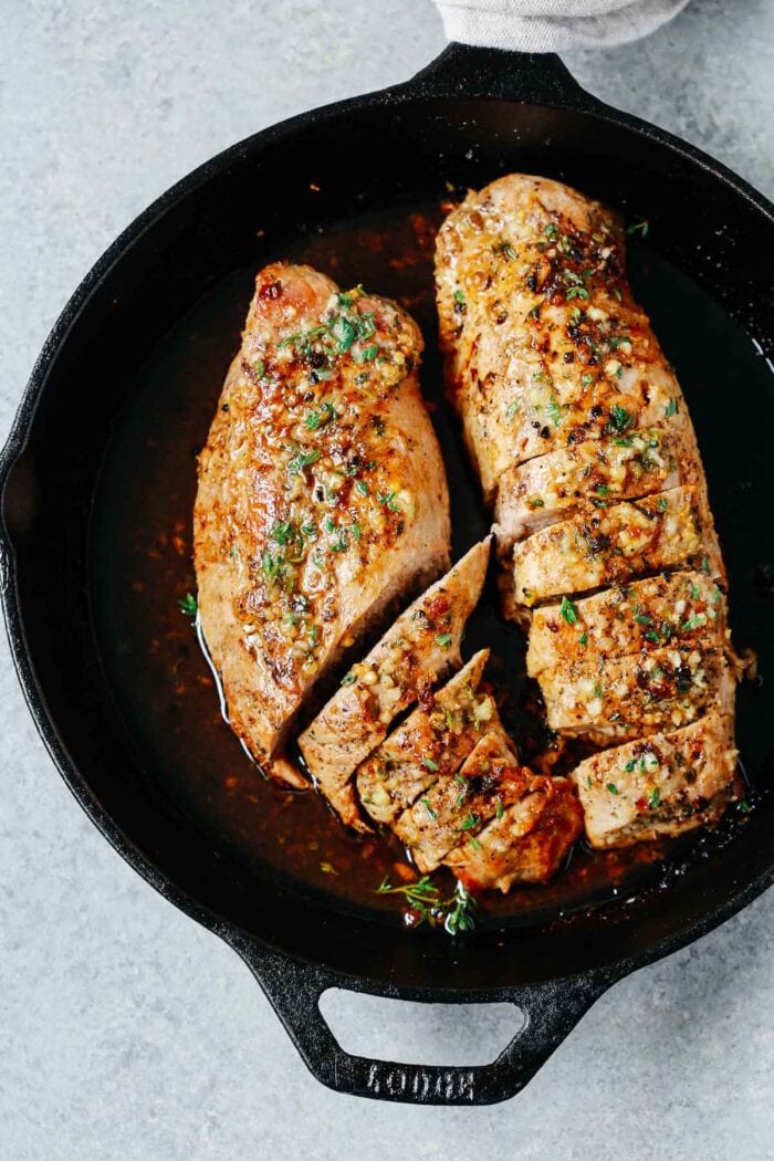 Cast iron pan holding two large pork tenderloins marinated in garlic butter and seasonings