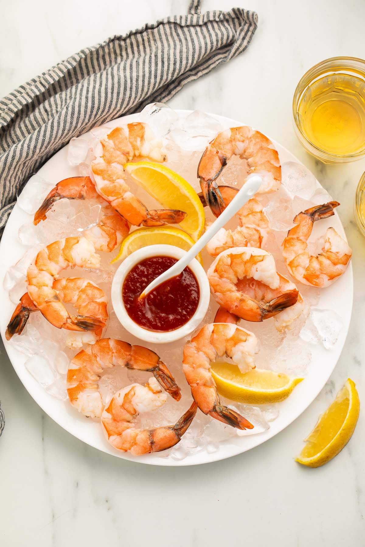 Poached shrimp arranged on a platter of ice next to a small dipping bowl of shrimp cocktail sauce.