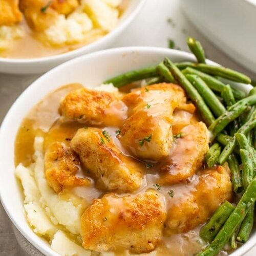 Whole30 fried chicken and mashed potatoes with gravy and green beans in a white ceramic bowl