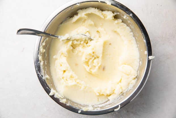 Mashed red potatoes in a medium silver saucepan on a white countertop.