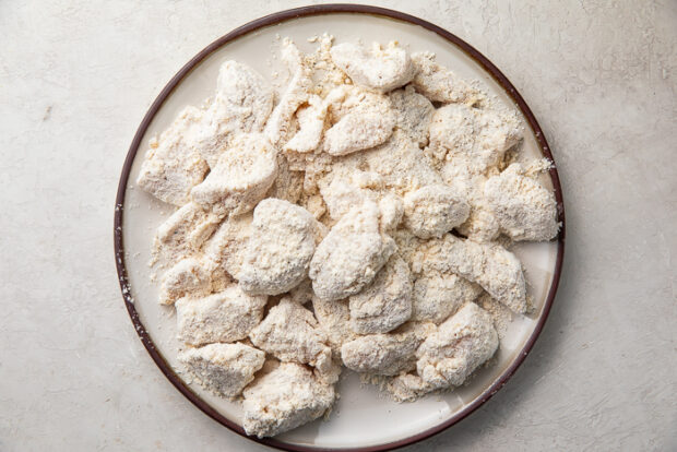 Flour coated chicken breast chunks on a white plate with brown edges