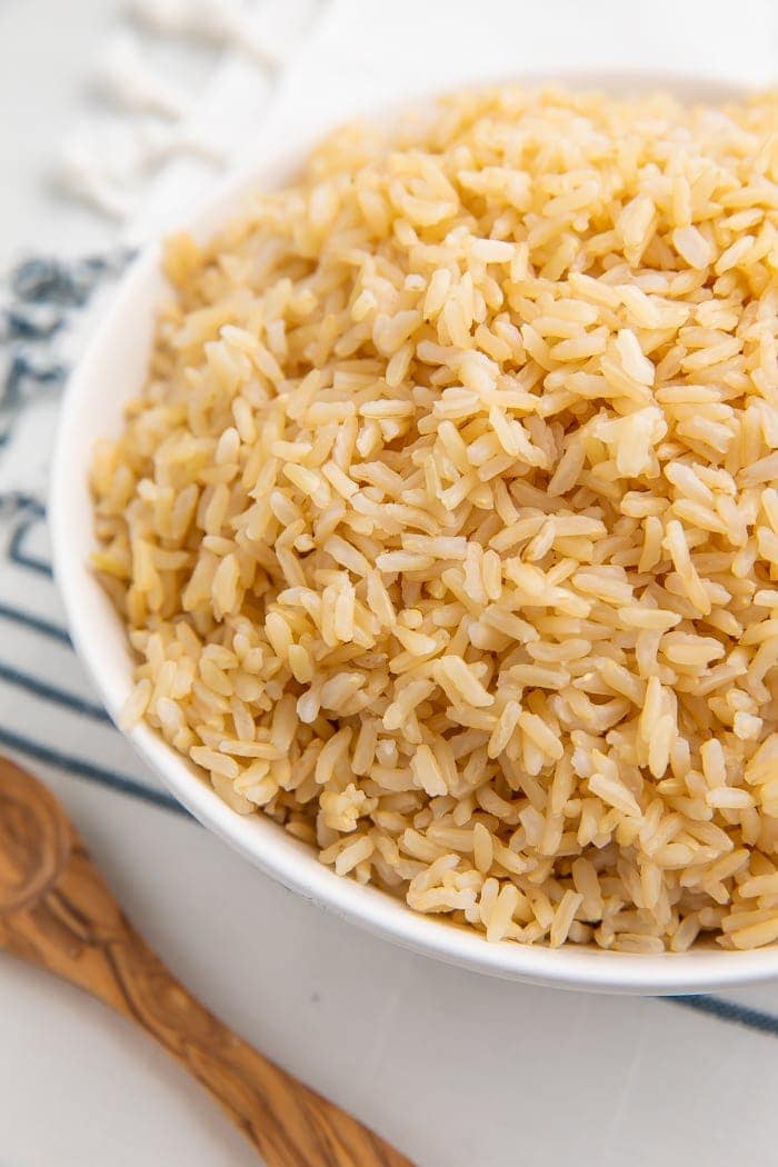 Partial image of a white bowl with brown rice on a blue striped dish towel