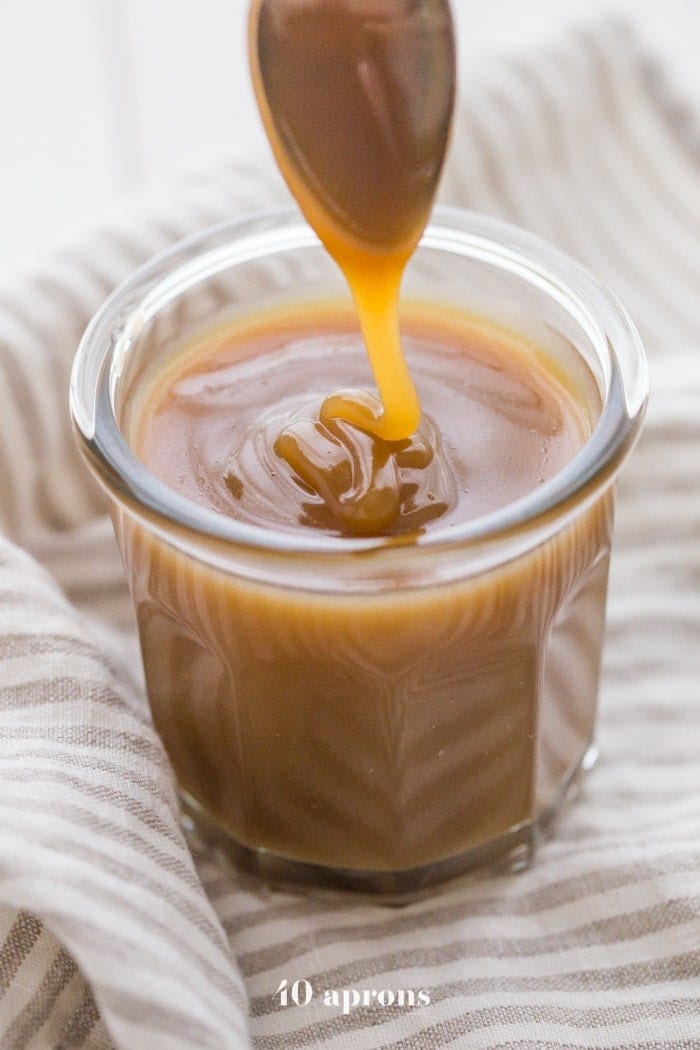 Vegan Instant Pot caramel sauce drizzling off a spoon into a glass jar of caramel sauce