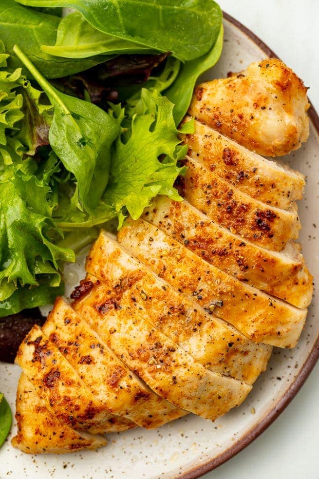 Air fried chicken breast on a white plate next to a bed of lettuce