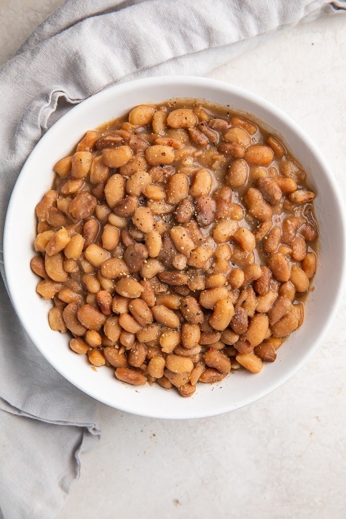 Zoomed out overhead photo of vegan Instant Pot pinto beans in a white bowl on a marble countertop