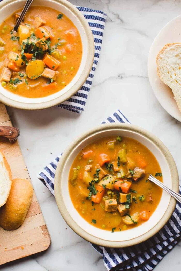 Tofu and potato stew in white bowls on striped napkins on a white countertop