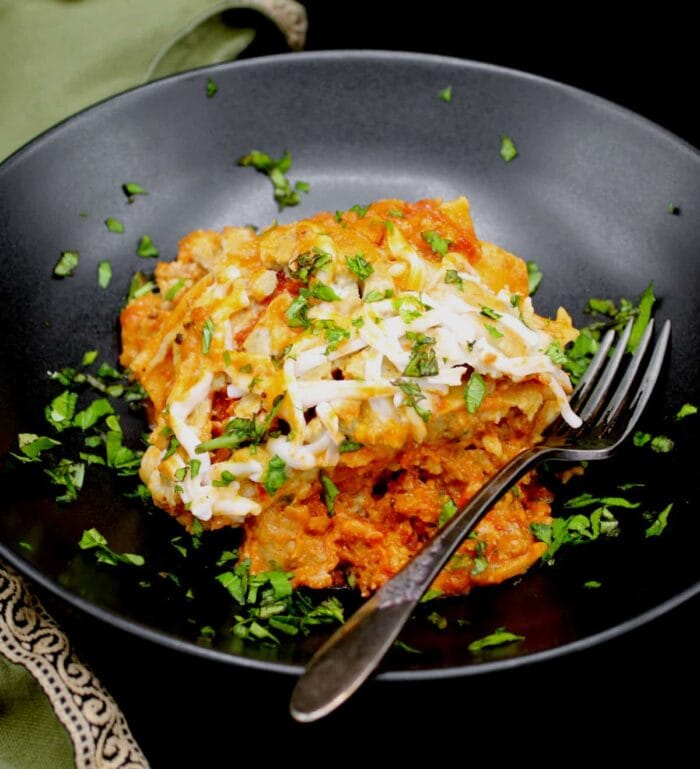 A square of vegan lasagna in a large black bowl with a fork