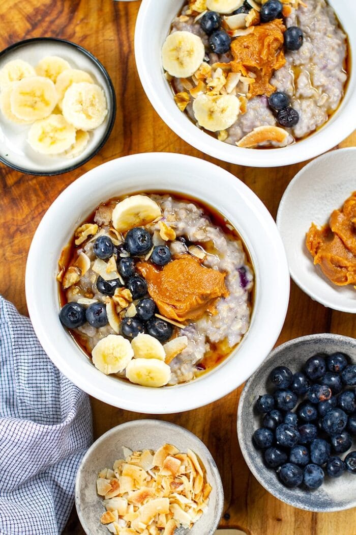 Two bowls of oatmeal with blueberries, peanut butter, and maple syrup