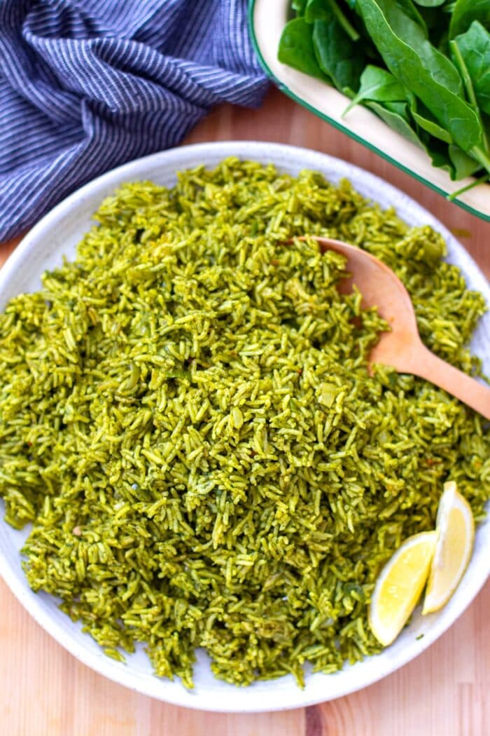 A white plate of spinach rice with a wooden spoon and a blue towel