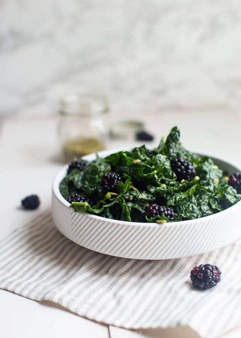 A white bowl containing lemon-garlic kale salad with blackberries