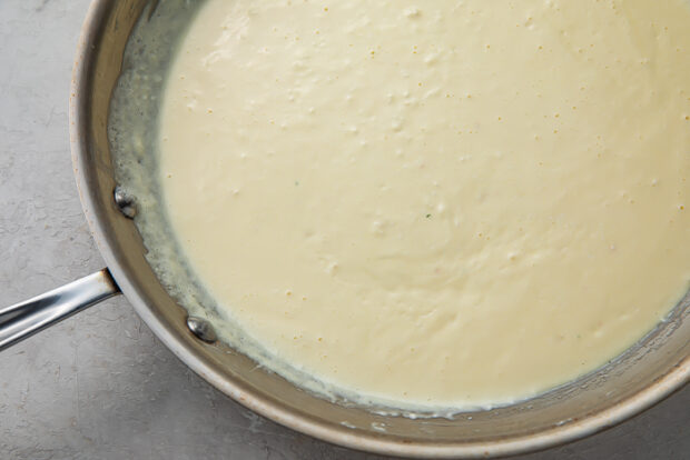 Heavy cream and melted cream cheese in stainless steel saucepan on white background