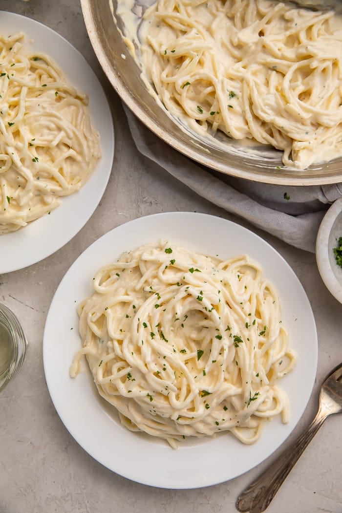 Two white plates and a silver saucepan full of palmini noodles with keto alfredo sauce