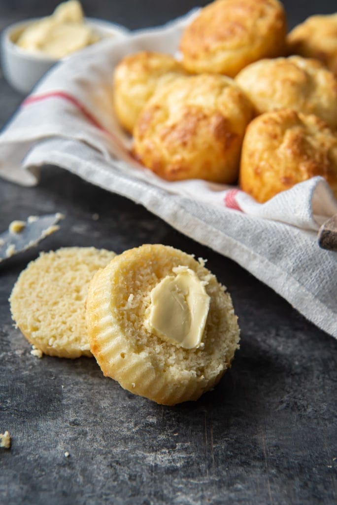 A keto biscuit cut in half, in front of a basket of keto biscuits