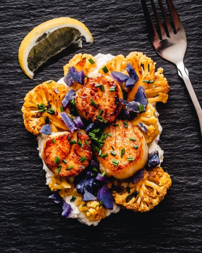 Sous vide scallops, cauliflower, and brown butter tahini sauce on a dark surface