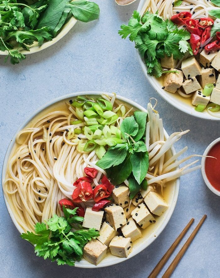 A white bowl of vegan Instant Pot pho on a blue background with other bowls