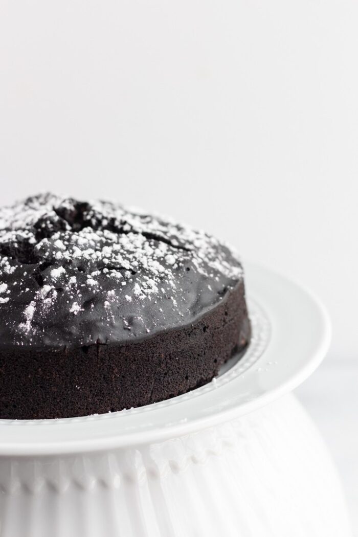 Half of a vegan chocolate cake on a white cake stand with a white background