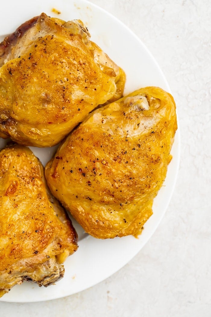 Three large chicken thighs on a white plate