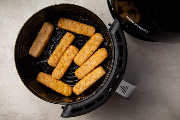 Frozen fish sticks in a black air fryer basket