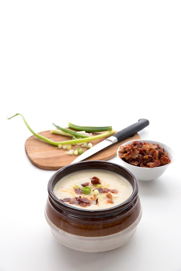 Bowl of cauliflower soup in front of bowls of garnish against a white backdrop