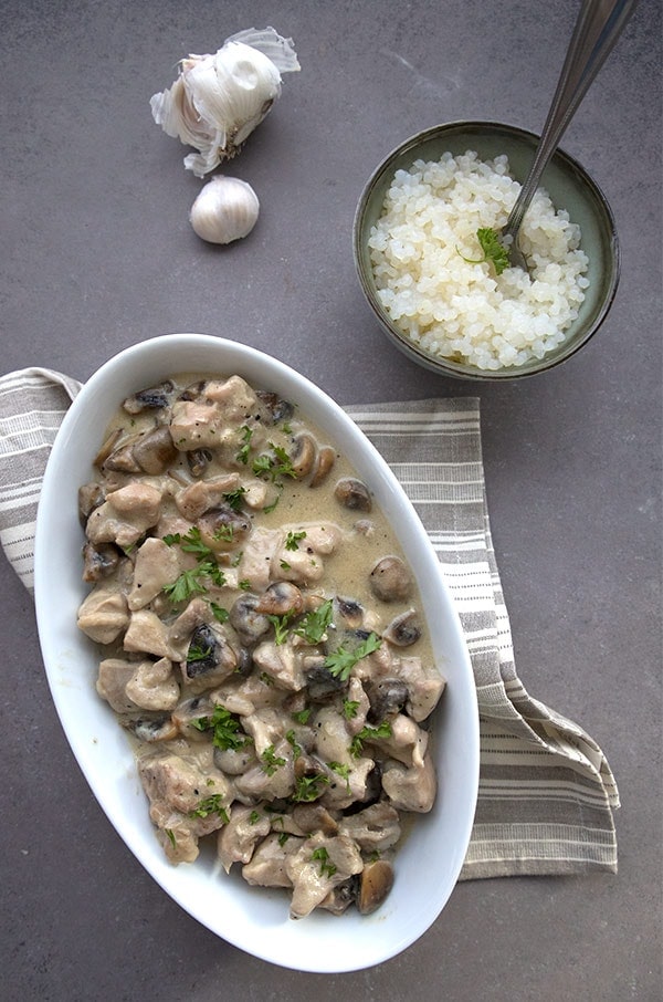 A white boat dish with chicken and mushrooms on a dark countertop