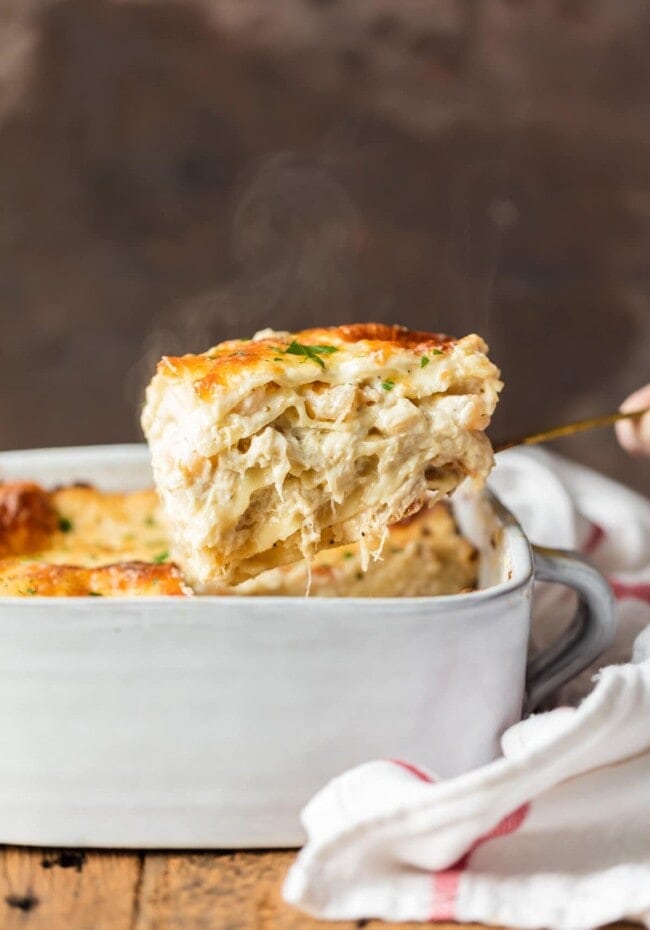 A square piece of seafood lasagna being lifted out of a white casserole dish with a spatula