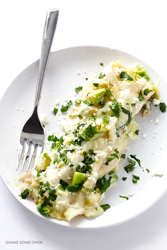 An enchilada garnished with avocado on a white plate