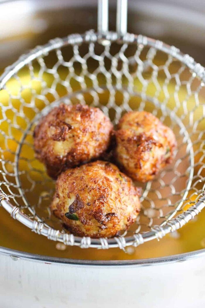 Three fried beignet balls in a fry basket, being held over a pot of frying oil