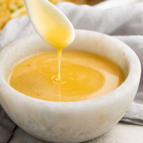 A spoon drizzling lemon butter sauce into a stone bowl