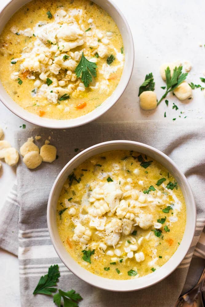 2 white bowls of chowder on a light tablecloth with oyster crackers