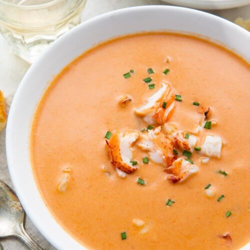 A large white bowl full of orange bisque with chunks of lobster, taken from an overhead angle