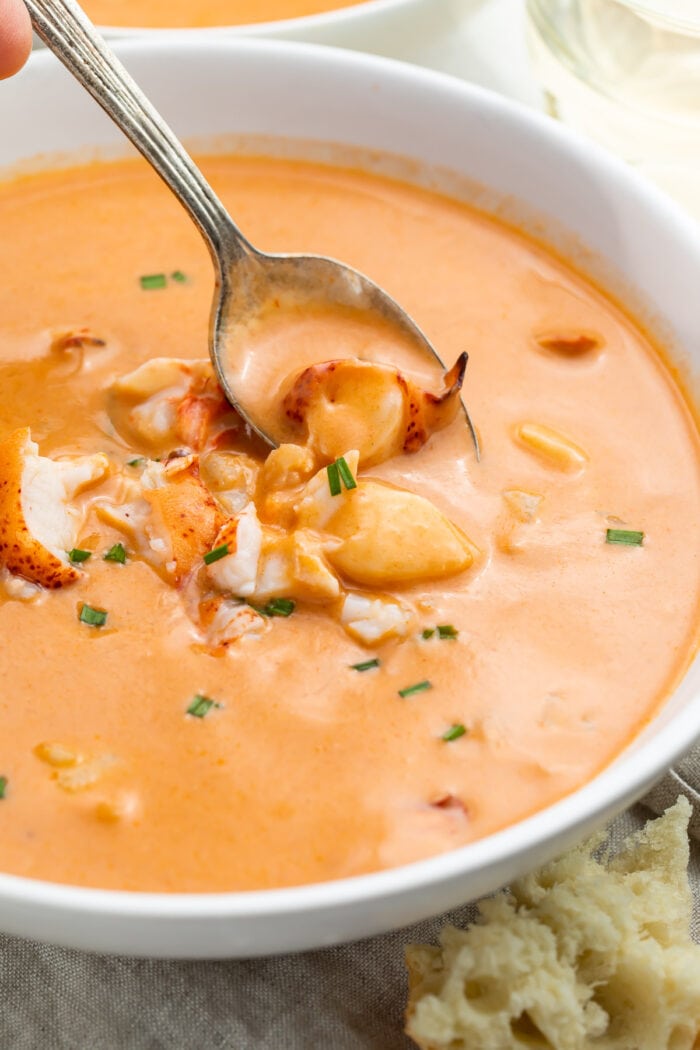 Close up of chunks of lobster tail in an orange lobster bisque in a white bowl