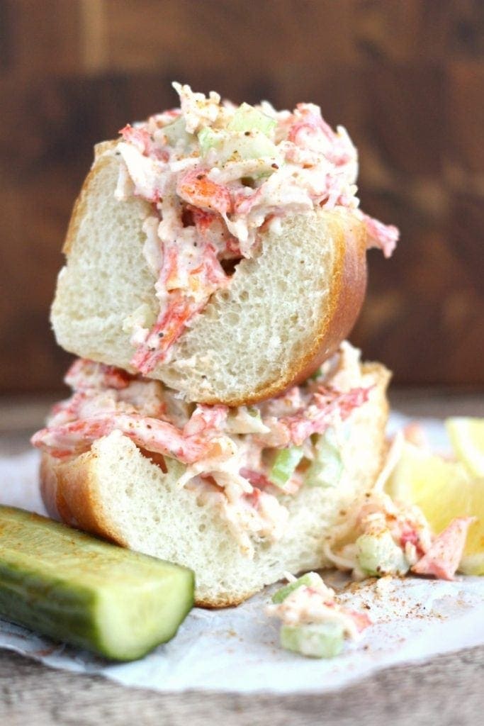 Two halves of a crab poboy, one stacked on top of the other, with a pickle on the side