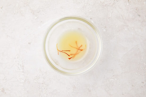 A small glass bowl containing chicken stock and saffron threads for seasoning mushroom risotto