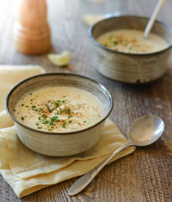 Two bowls of soup on a wooden table, one bowl sitting on a tan napkin